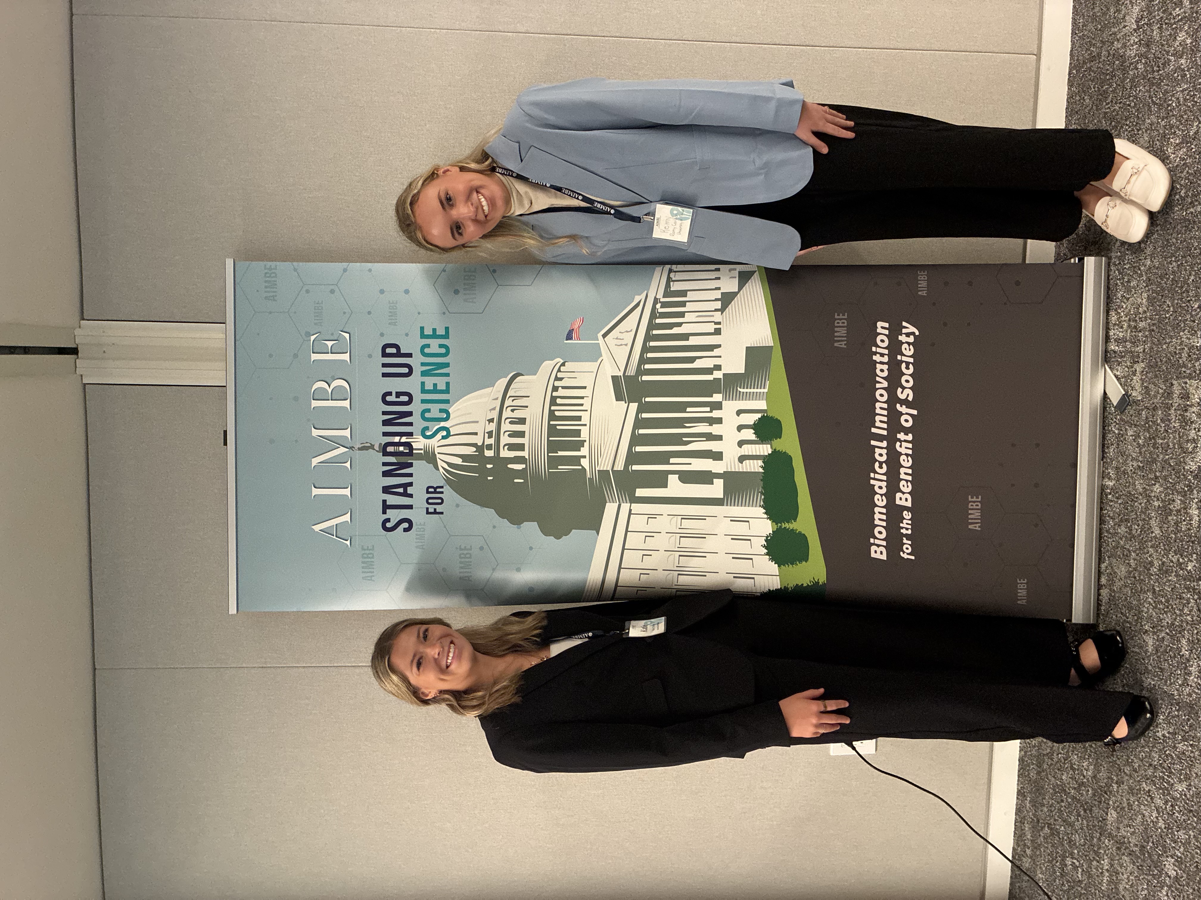 Remy Carlson and Katie Childers beside the AIMBE Standing Up for Science banner
